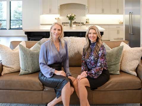 Two women sitting on a couch, posing for a photo